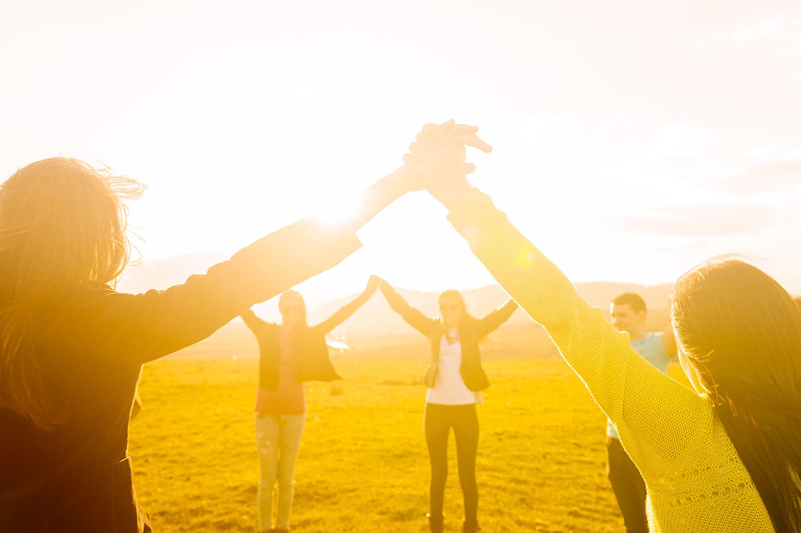 Circle of people joining hands in a field.